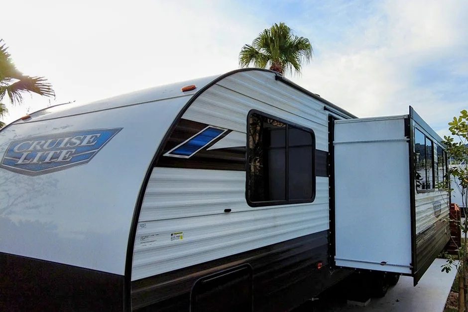 パームツリーが見える屋外に駐車された、白と黒の「CRUISE LITE」と書かれたキャンピングカーの側面
