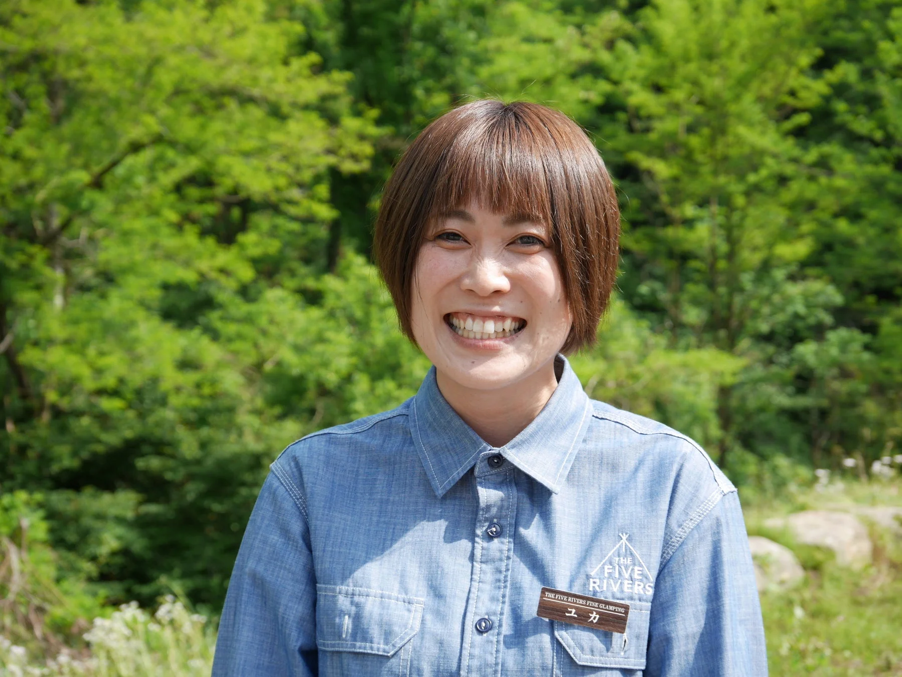 緑豊かな自然を背景に、デニムシャツを着た女性