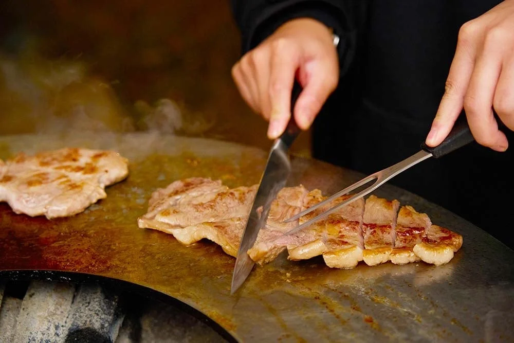 熱い鉄板の上で肉を切り分けるシェフ