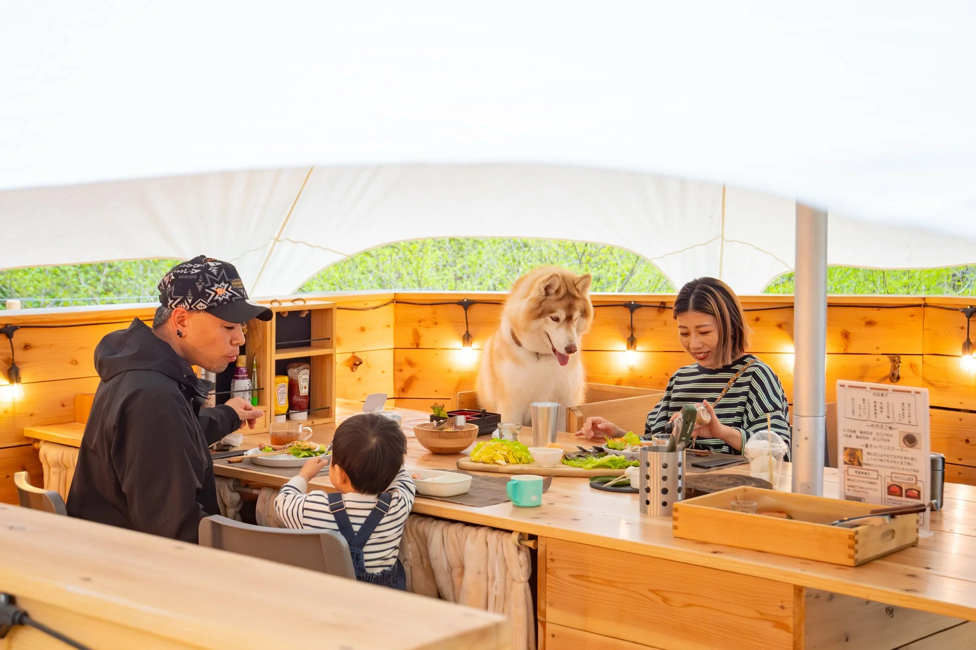グランピング施設で、家族とハスキー犬が一緒に食事を楽しんでいる様子