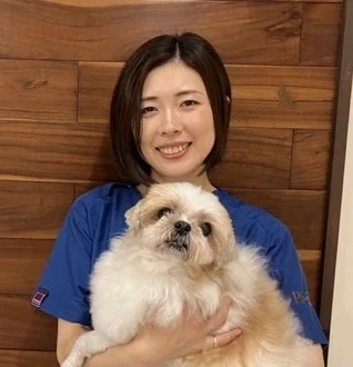 青い制服を着た女性が、笑顔でふわふわした小型犬を抱いている