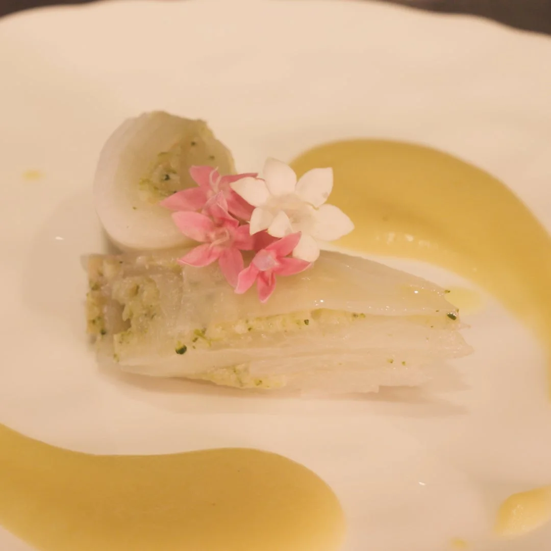 白菜のような野菜が美しく層になって盛り付けられ、丸い野菜と可憐な花々で飾られたエレガントな一皿