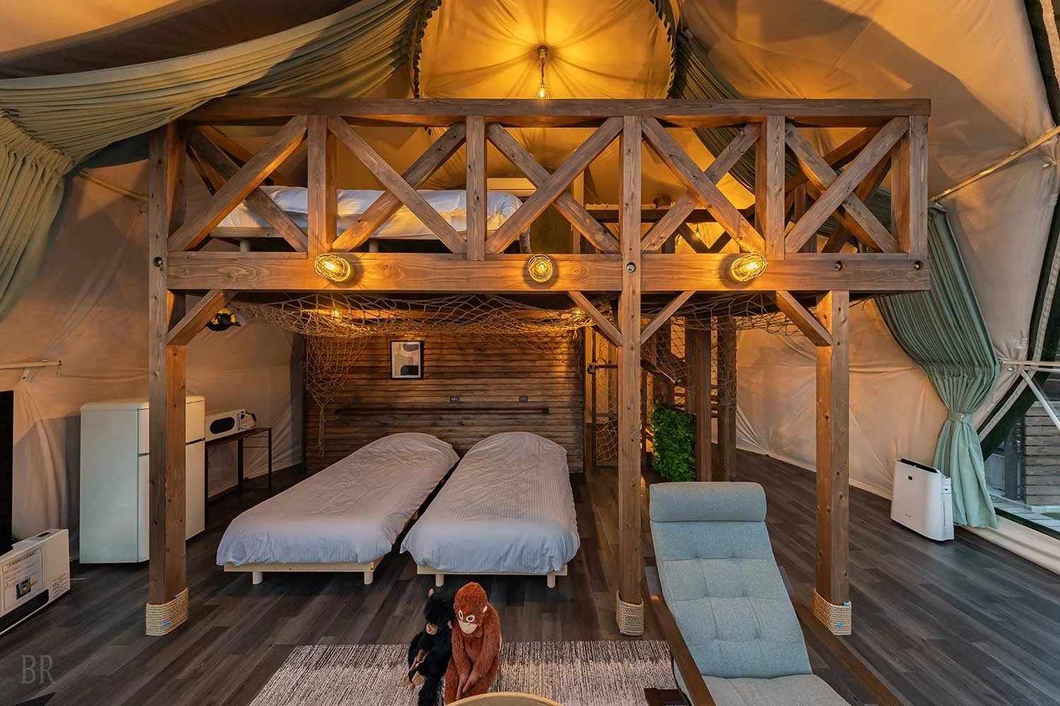 ロフトベッドのある広々としたグランピングテントの内部で、木製の温かみとモダンなデザインが融合した快適な宿泊空間