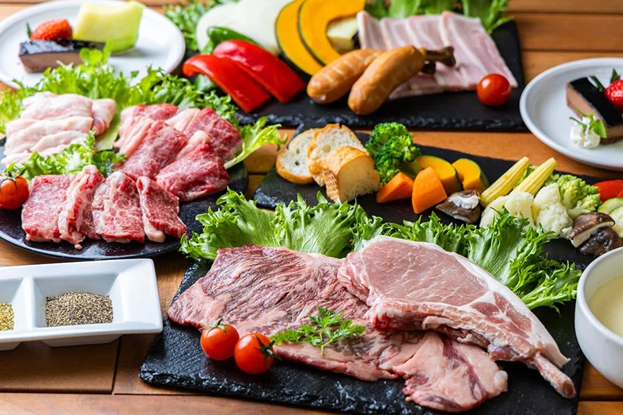 牛肉、豚肉、ソーセージ、ベーコンなど様々な肉類と、彩り豊かな新鮮な野菜が豊富に盛り付けられた豪華な食材の準備風景