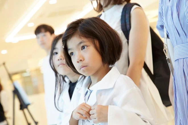 白衣を着た幼い女の子が真剣な表情で何かを見つめている様子