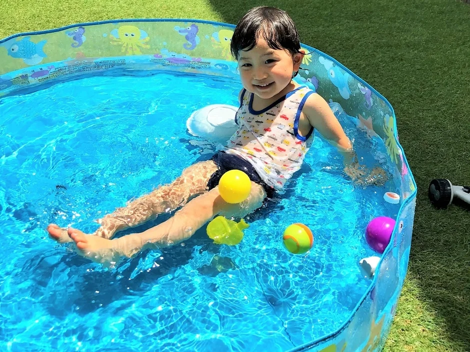 青いビニールプールで水遊びを楽しむ子供