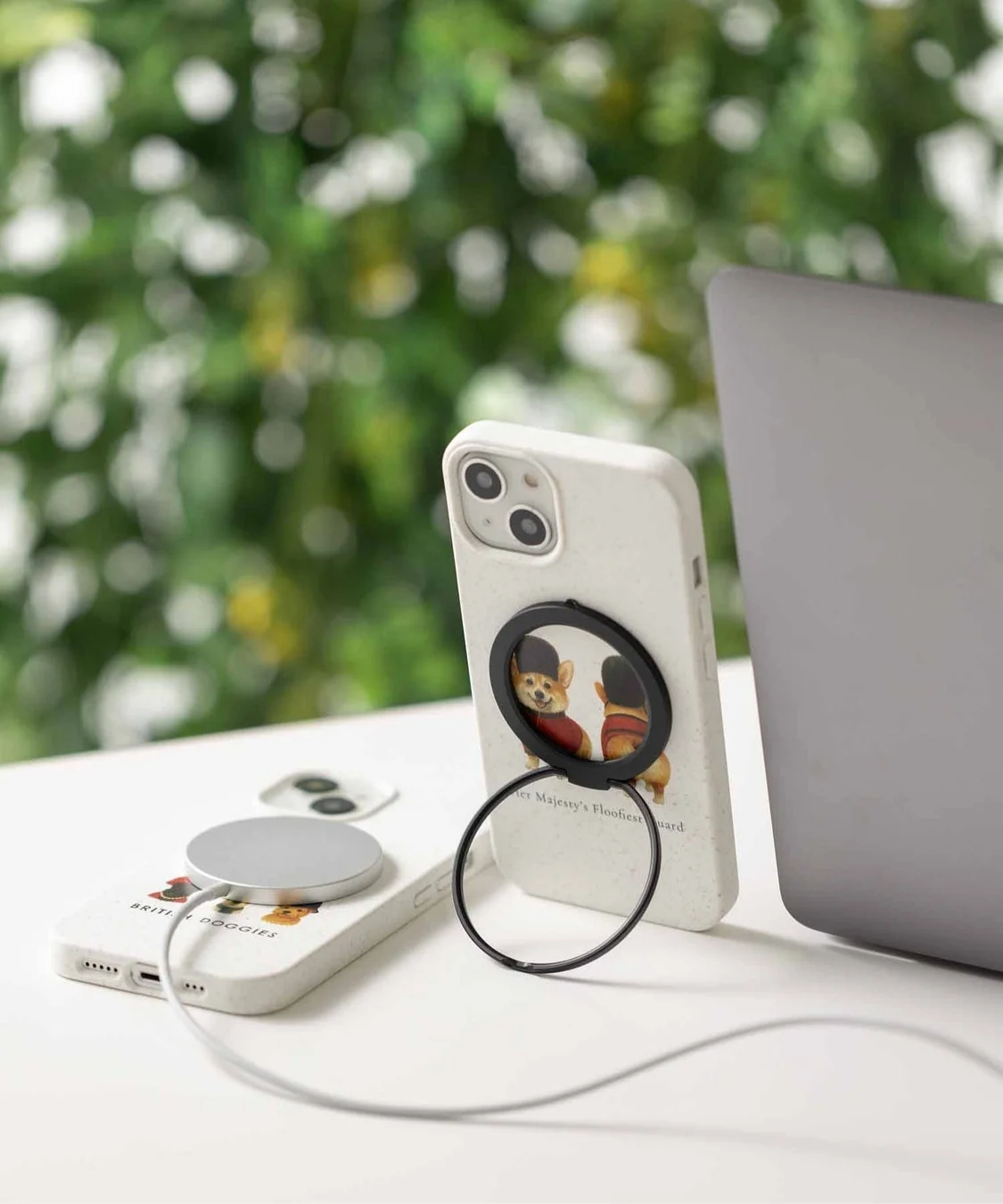 白いコーギー柄のスマホケースを装着した2台のiPhoneが写っています。1台はMagSafeでワイヤレス充電中で、もう1台はリングスタンドで立てられています。