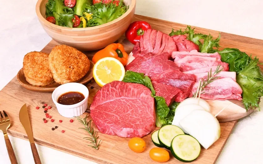 木製のボードに豪華な焼肉セットが美しく盛り付けられています。霜降りの牛肉、新鮮なレタスやトマトのサラダ、焼きおにぎり、様々な野菜。