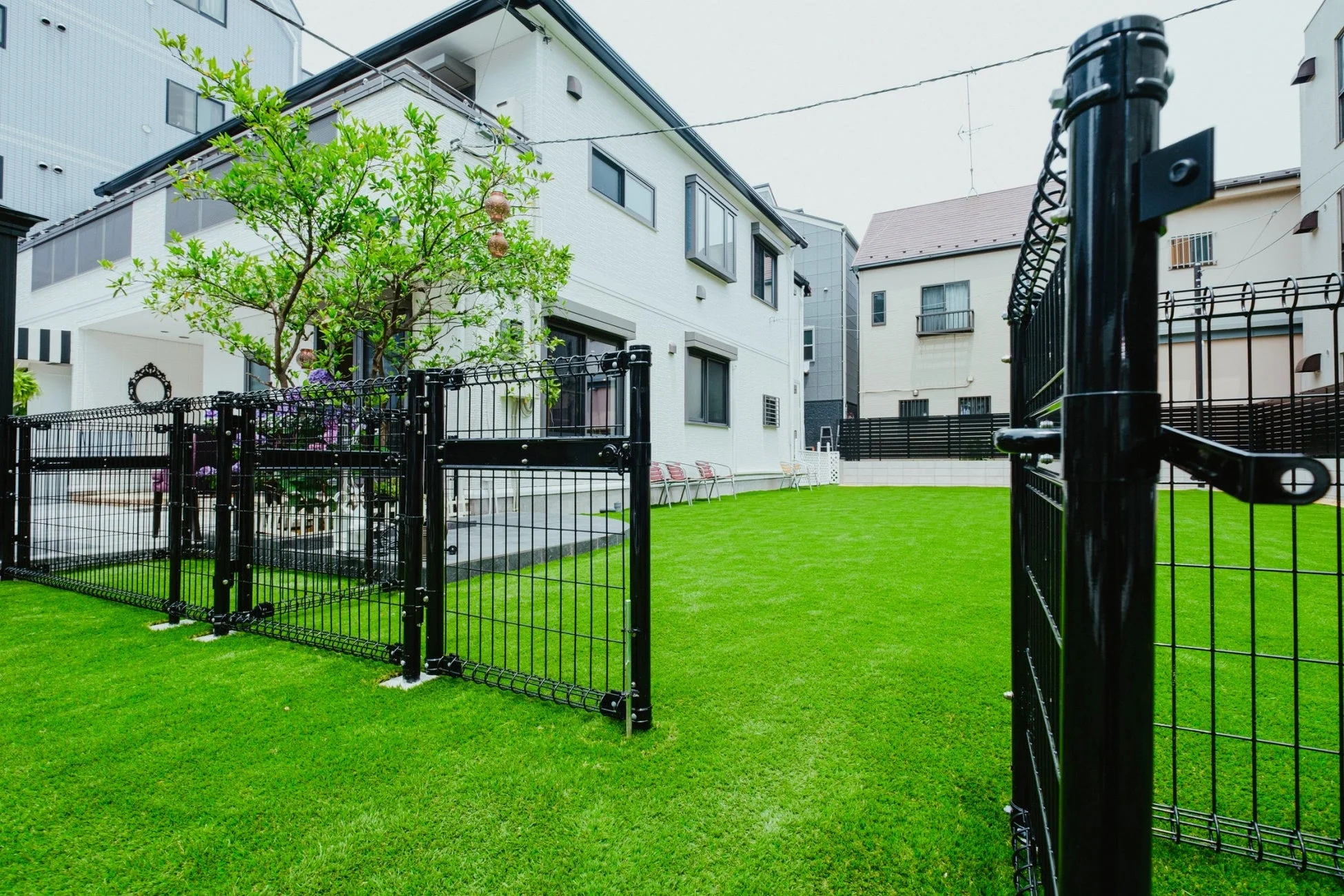 白いモダンな一戸建て住宅の庭に広がる鮮やかな人工芝と黒いフェンスが特徴的な風景
