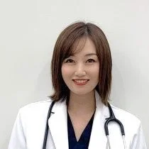 白衣を着て聴診器を首にかけた、笑顔の女性医師の胸から上のポートレートです。