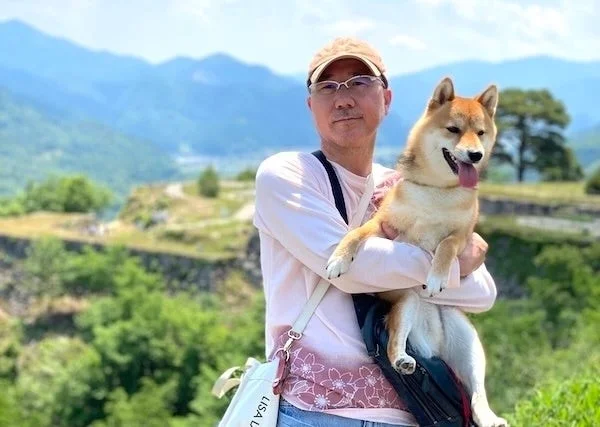 男性が柴犬を抱っこしてカメラに微笑みかけている。