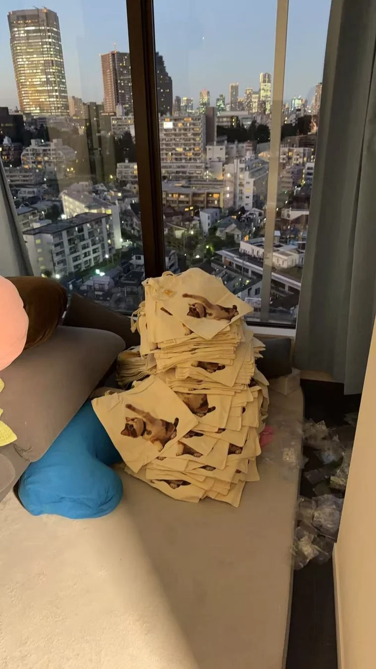 窓の外に夜景が広がる部屋で、積み重ねられたトートバッグ