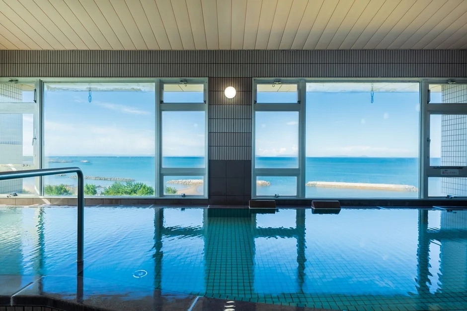 大きな窓から青い海と空が広がる室内プールまたは温泉浴場