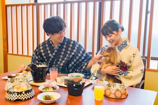 浴衣を着たカップルが、犬を連れて和風の宿で食事を楽しんでいる様子