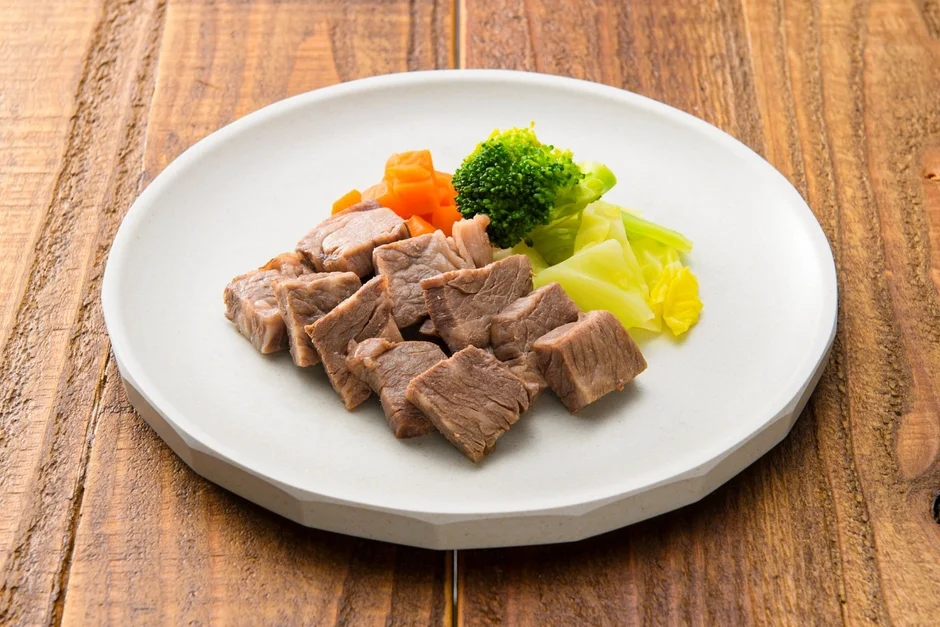 白い皿に、角切りにされた煮込み肉と、ブロッコリー、人参、キャベツが盛り付けられた、バランスの取れた一品