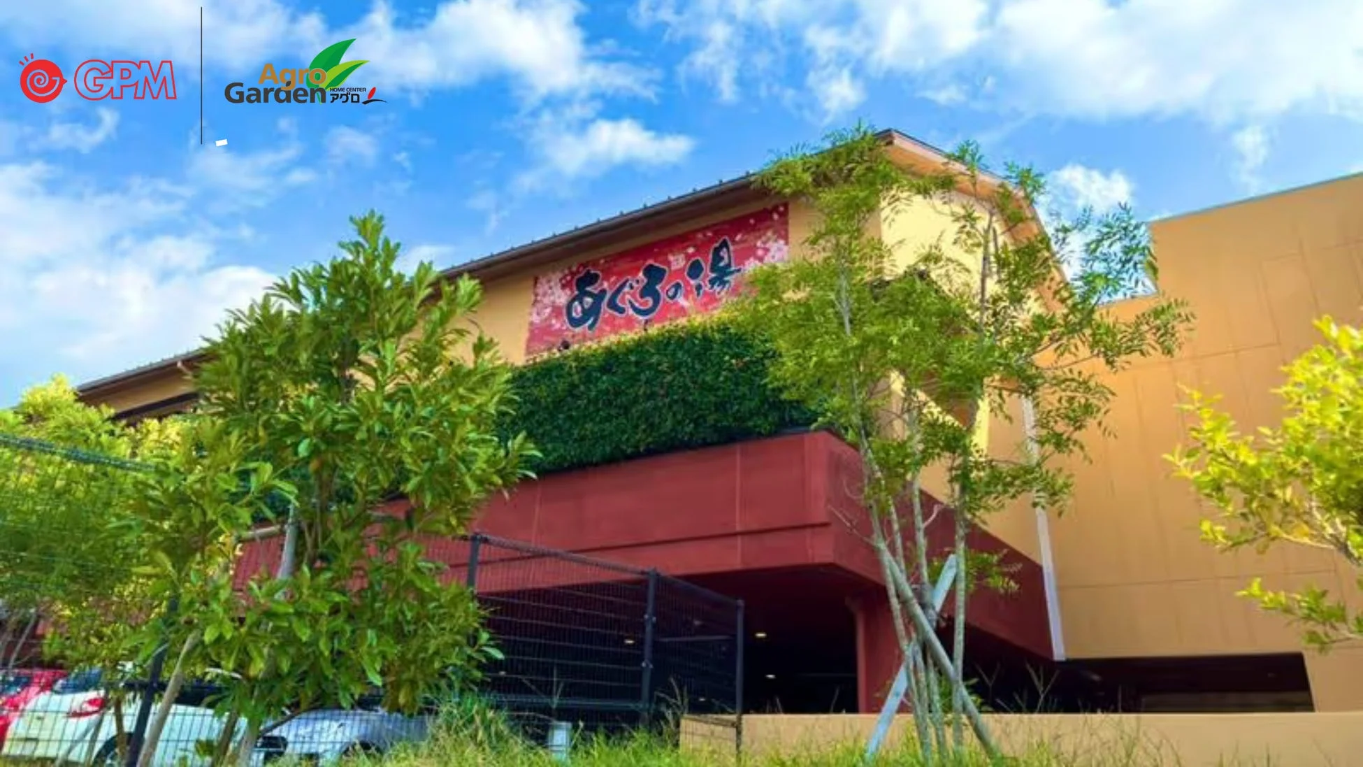 青空の下に建つ「あぐろの湯」の建物。上部にはGPMとアグロガーデンのロゴが見える。周囲には緑豊かな木々が配置され、駐車場らしきスペースに車が停まっている様子も伺える。