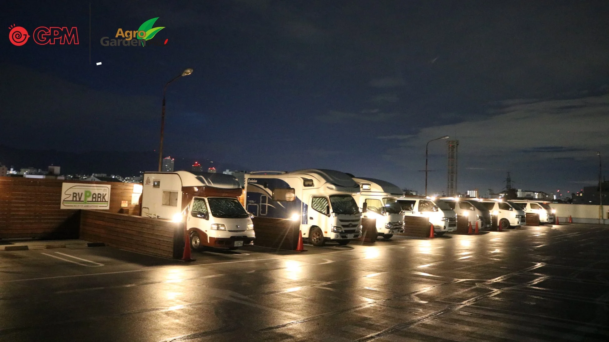 夜のRVパークに多数のキャンピングカーが駐車している様子を捉えた画像です。街の明かりが遠くに見え、落ち着いた雰囲気が漂っています。