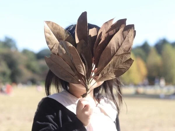 枯れ葉で顔を隠す人物